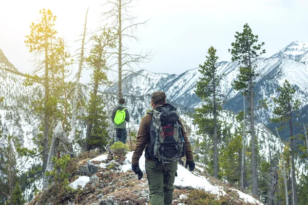 Los hombres excursionistas con mochila en la cima de la montaña mirando a la pendiente de la nieve. Concepto de motivación y logro de metas — Foto de Stock