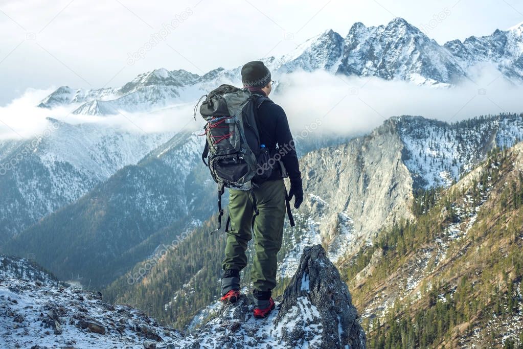 Man hiker with backpack on top of the mountain back, looking at the snow slope. Concept motivation and goal achievement