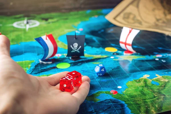 Hand throwing red dice on the world map of the playing field handmade Board games with a pirate ship — Stock Photo, Image