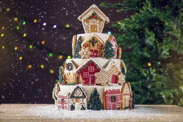 Large tiered Christmas cake decorated with gingerbread cookies and a house on top. Tree and garlands in the background. — Stock Photo, Image