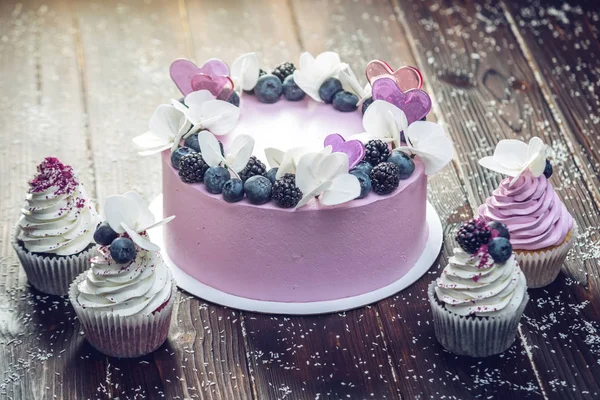 Hermoso pastel morado decorado con bayas, moras y arándanos en la parte superior con cupcakes en la mesa festiva —  Fotos de Stock