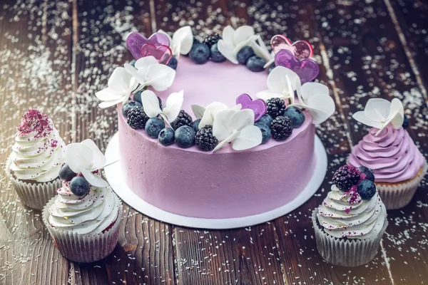Hermoso pastel morado decorado con bayas, moras y arándanos en la parte superior con cupcakes en la mesa festiva —  Fotos de Stock