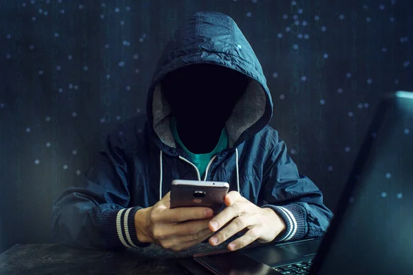 Seorang peretas anonim tanpa wajah menggunakan ponsel untuk meretas sistem. Konsep kejahatan dunia maya Stok Gambar