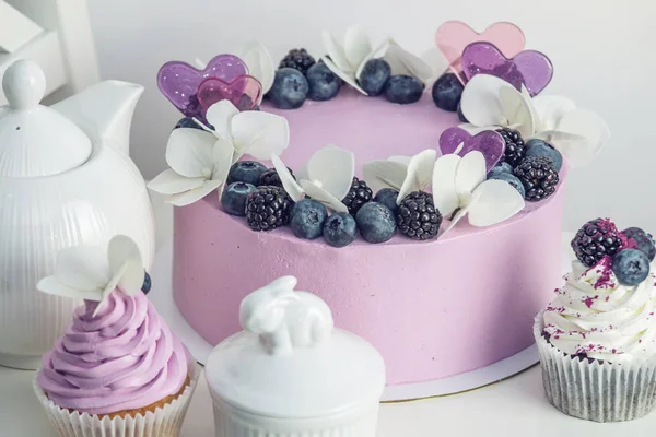 Bolo bonito roxo decorado com bagas, amoras e mirtilos em cima com cupcakes na mesa festiva — Fotografia de Stock