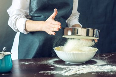 Siyah önlük Şef un hamur pizza için hazırlamak için bir elek ile sifts