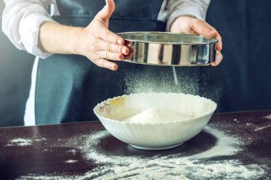 Siyah önlük Şef un hamur pizza için hazırlamak için bir elek ile sifts