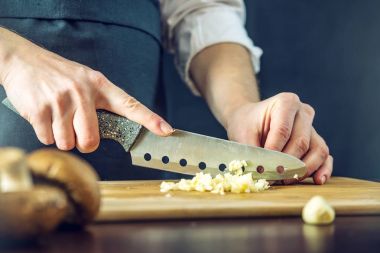 Siyah önlük Şef sarımsak bıçakla keser. Yemek pişirmek için çevre dostu ürünler kavramı