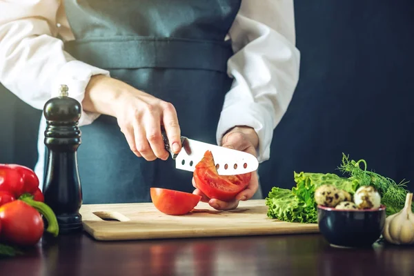 El chef en delantal negro corta verduras. Concepto de productos ecológicos para cocinar — Foto de Stock