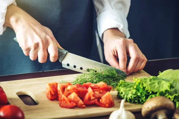El chef en delantal negro corta verduras. Concepto de productos ecológicos para cocinar — Foto de Stock