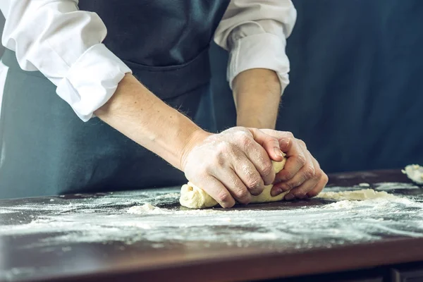 Шеф-повар в черном фартуке делает тесто для пиццы с руками на столе. — стоковое фото