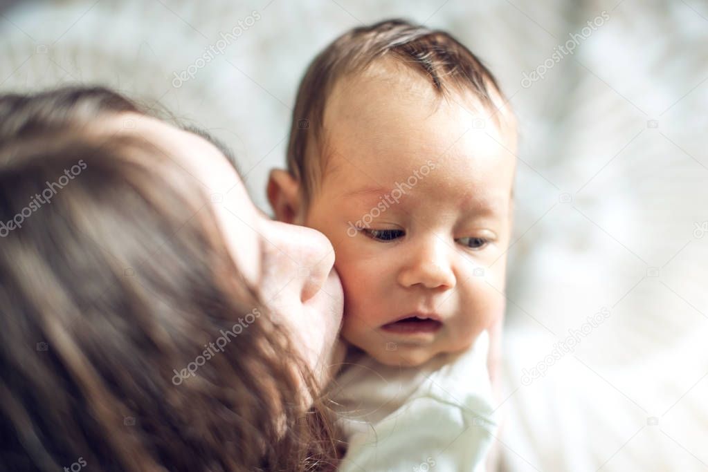 Happy caring mother holding baby boy in the bedroom. The concept of the tenderness of motherhood and family values