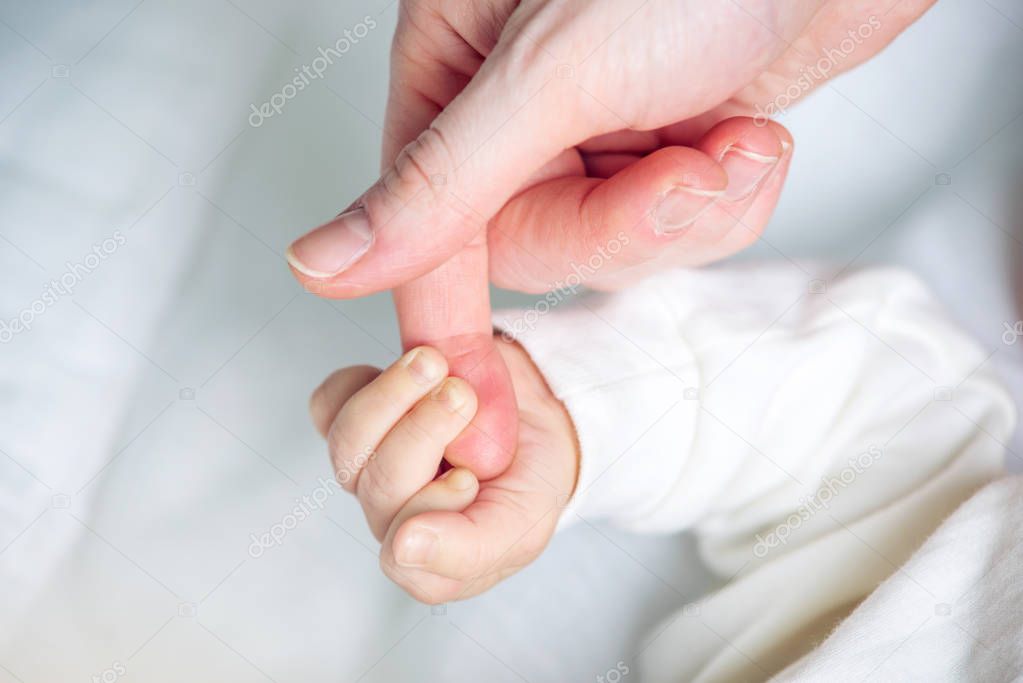 Baby boy holding mother's hand, squeezes the fingers. The concept of empathy, trust, care and tenderness of motherhood
