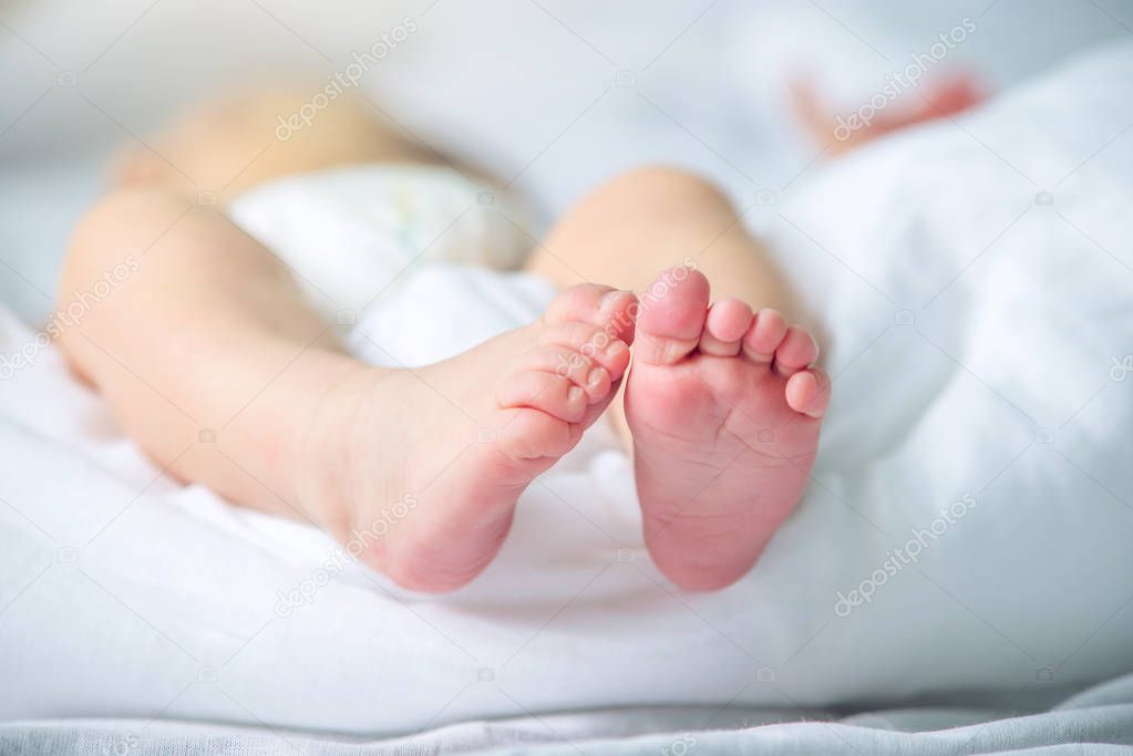 Baby feet with pink lying on a white blanket. The concept of tenderness and motherhood