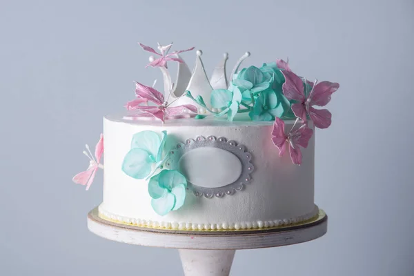 Vacker vit tårta dekorerad med rosa och turkosa blommor och en prinsessa krona. Begreppet desserter för flickor — Stockfoto