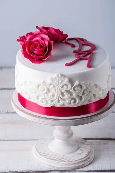 美しい白いウエディング ケーキ花赤いバラやリボンで装飾されています。エレガントな休日のデザートのコンセプト — ストック写真