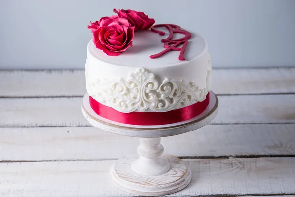 Schöne weiße Hochzeitstorte mit Blumen, roten Rosen und Schleife dekoriert. Konzept der eleganten Urlaubsdesserts — Stockfoto