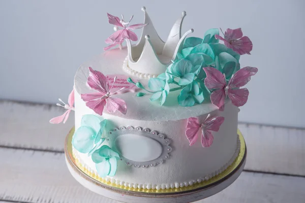 खूबसूरत सफेद केक गुलाबी और फ़िरोज़ा फूलों और एक राजकुमारी मुकुट के साथ सजाया। लड़कियों के लिए मिठाई की अवधारणा — स्टॉक फ़ोटो, इमेज