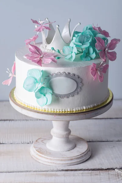 Beautiful white cake decorated with pink and turquoise flowers and a Princess crown. Concept of desserts for girls