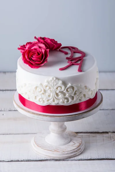 Hermoso pastel de boda blanco decorado con flores rosas rojas y cinta. Concepto de elegantes postres navideños — Foto de Stock
