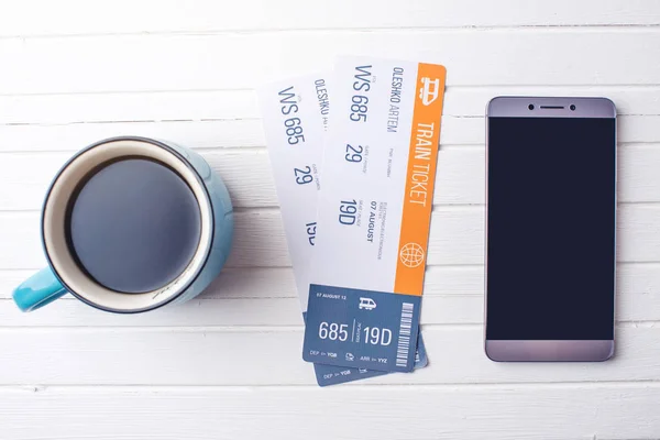 Cup of coffee train tickets and phone on white wooden background. Concept of buying the online ticket booking — Stock Photo, Image