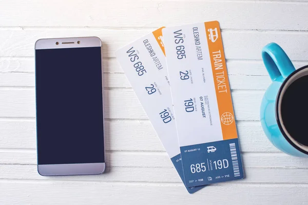 Cup of coffee train tickets and phone on white wooden background. Concept of buying the online ticket booking