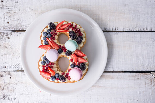 Торт в форме цифры 8 украшен белым кремом и ягодами. Сладкий десерт в подарок к женскому дню марта
