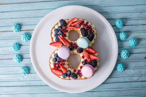 Торт в форме цифры 8 украшен белым кремом и ягодами. Сладкий десерт в подарок к женскому дню марта
