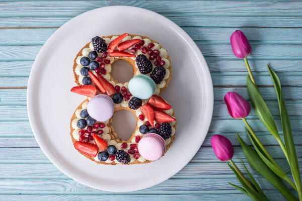 Торт в форме номера 8, украшенный ягодами и цветами тюльпанов. Десерт на женский день 8 марта
