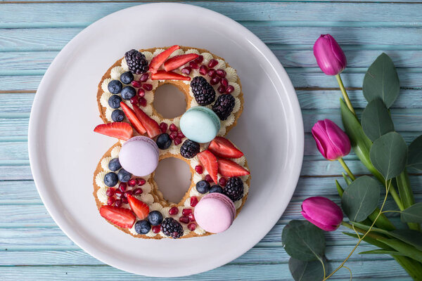 Торт в форме номера 8, украшенный ягодами и цветами тюльпанов. Десерт на женский день 8 марта
