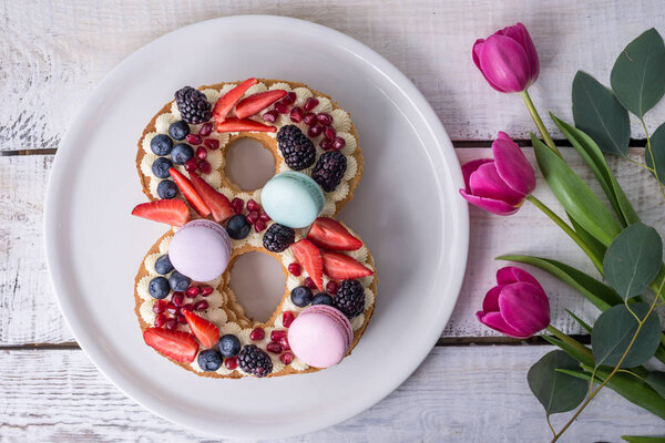 Торт в форме номера 8, украшенный ягодами и цветами тюльпанов. Десерт на женский день 8 марта
