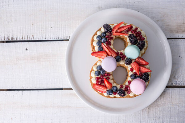 Торт в форме цифры 8 украшен белым кремом и ягодами. Сладкий десерт в подарок к женскому дню марта
