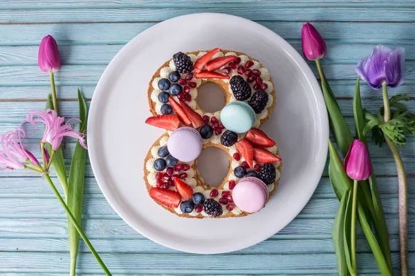 Торт в форме номера 8, украшенный ягодами и цветами тюльпанов. Десерт на женский день 8 марта — стоковое фото