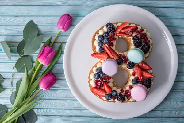 Торт в форме номера 8, украшенный ягодами и цветами тюльпанов. Десерт на женский день 8 марта — стоковое фото