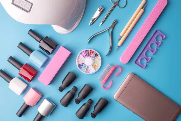 Conjunto de herramientas cosméticas para manicura y pedicura sobre fondo azul. Esmaltes de gel, limas y cortauñas, vista superior — Foto de Stock
