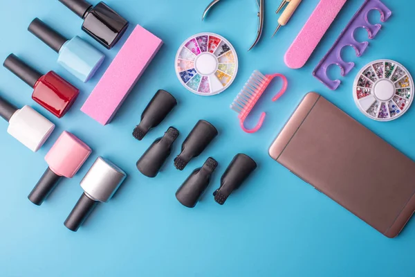 Conjunto de herramientas cosméticas para manicura y pedicura sobre fondo azul. Esmaltes de gel, limas y cortauñas, vista superior — Foto de Stock