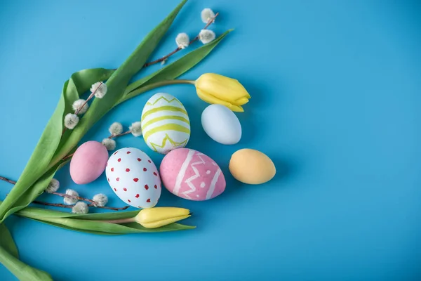 Ovos de Páscoa coloridos com tulipa amarela pintados à mão sobre um fundo azul. Cartão de primavera feriado — Fotografia de Stock