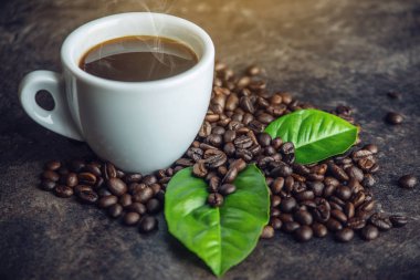 Beyaz Siyah espresso fincan kahve çekirdekleri ve yeşil yığını ile çanta içinde koyu arka plan üzerinde bırakır.