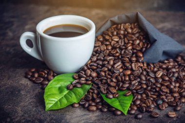 Beyaz Siyah espresso fincan kahve çekirdekleri ve yeşil yığını ile çanta içinde koyu arka plan üzerinde bırakır.