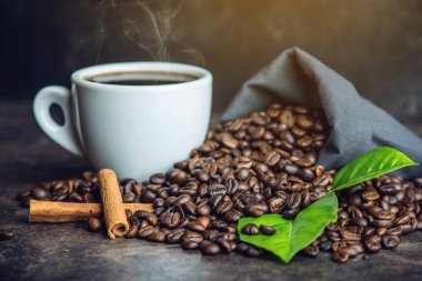 Beyaz Siyah espresso fincan kahve çekirdekleri ve yeşil yığını ile çanta içinde koyu arka plan üzerinde bırakır.