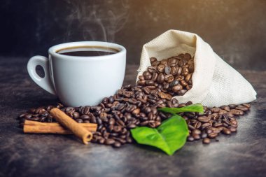 Beyaz Siyah espresso fincan kahve çekirdekleri ve yeşil yığını ile çanta içinde koyu arka plan üzerinde bırakır.