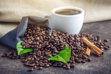 Beyaz Siyah espresso fincan kahve çekirdekleri ve yeşil yığını ile çanta içinde beyaz keten zemin üzerine bırakır.