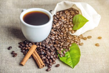 Beyaz Siyah espresso fincan kahve çekirdekleri ve yeşil yığını ile çanta içinde beyaz keten zemin üzerine bırakır.