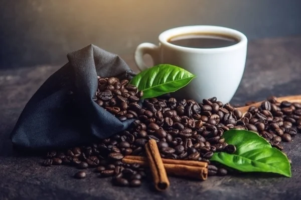 Taza de café negro blanco con un montón de granos de café y hojas verdes en el bolso sobre fondo oscuro —  Fotos de Stock