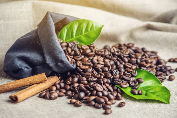 Montón de granos de café y hojas verdes en bolsa sobre fondo de lino blanco. Concepto de producción de bebidas frescas . —  Fotos de Stock