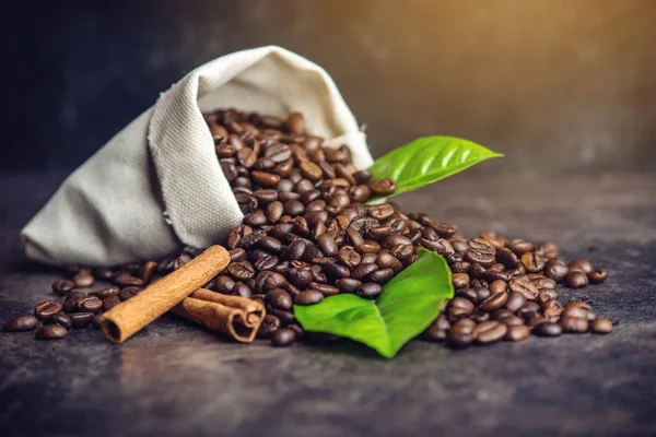 Montón de granos de café y hojas verdes en bolsa sobre fondo oscuro —  Fotos de Stock