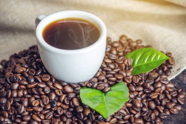 Beyaz Siyah espresso fincan kahve çekirdekleri ve yeşil yığını ile çanta içinde beyaz keten zemin üzerine bırakır.