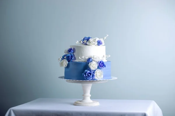 Wunderschöne zweistufige weiße und blaue Hochzeitstorte, die mit Blumen und Zuckerrosen dekoriert ist. Konzept der eleganten Urlaubsdesserts — Stockfoto