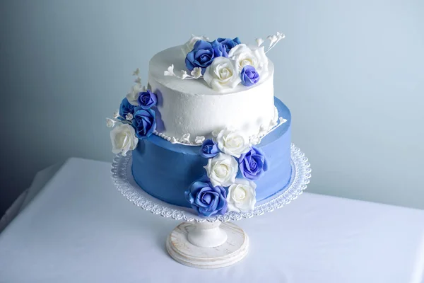 Gyönyörű két többszintű fehér és kék esküvői torta virágokkal díszített, cukor rózsák. Az elegáns holiday desszertek koncepció — Stock Fotó