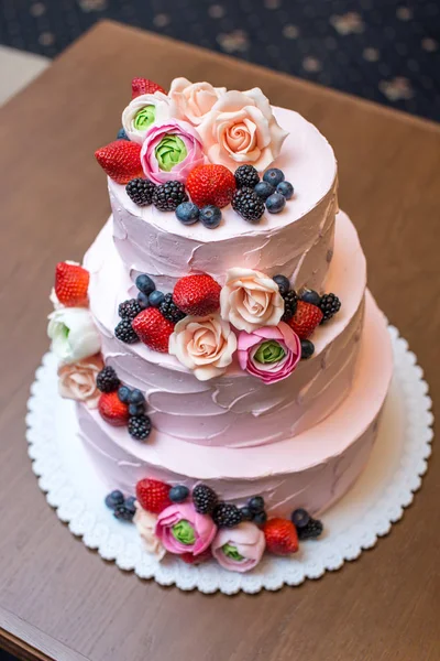 Три ярусных розовый свадебный торт украшен ягодами и цветами. Концепция кондитерской флористики из сахарной мастики — стоковое фото