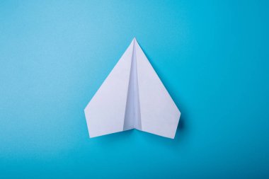 Pastel mavi zemin üzerine beyaz kağıt origami uçak yatıyor